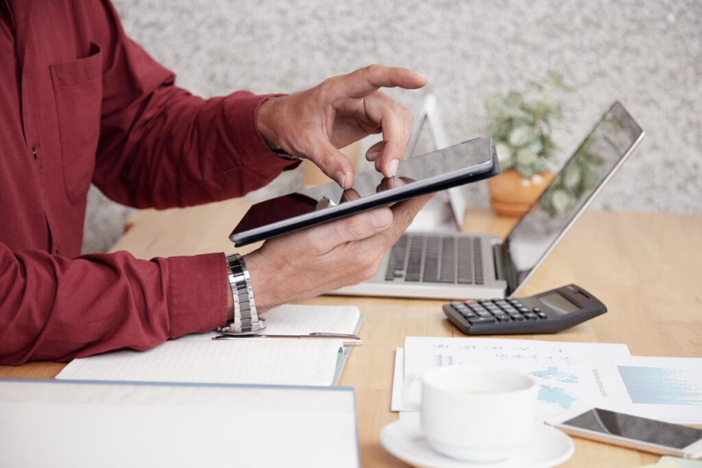 Close-up of businessman sitting at office desk and using digital tablet for work